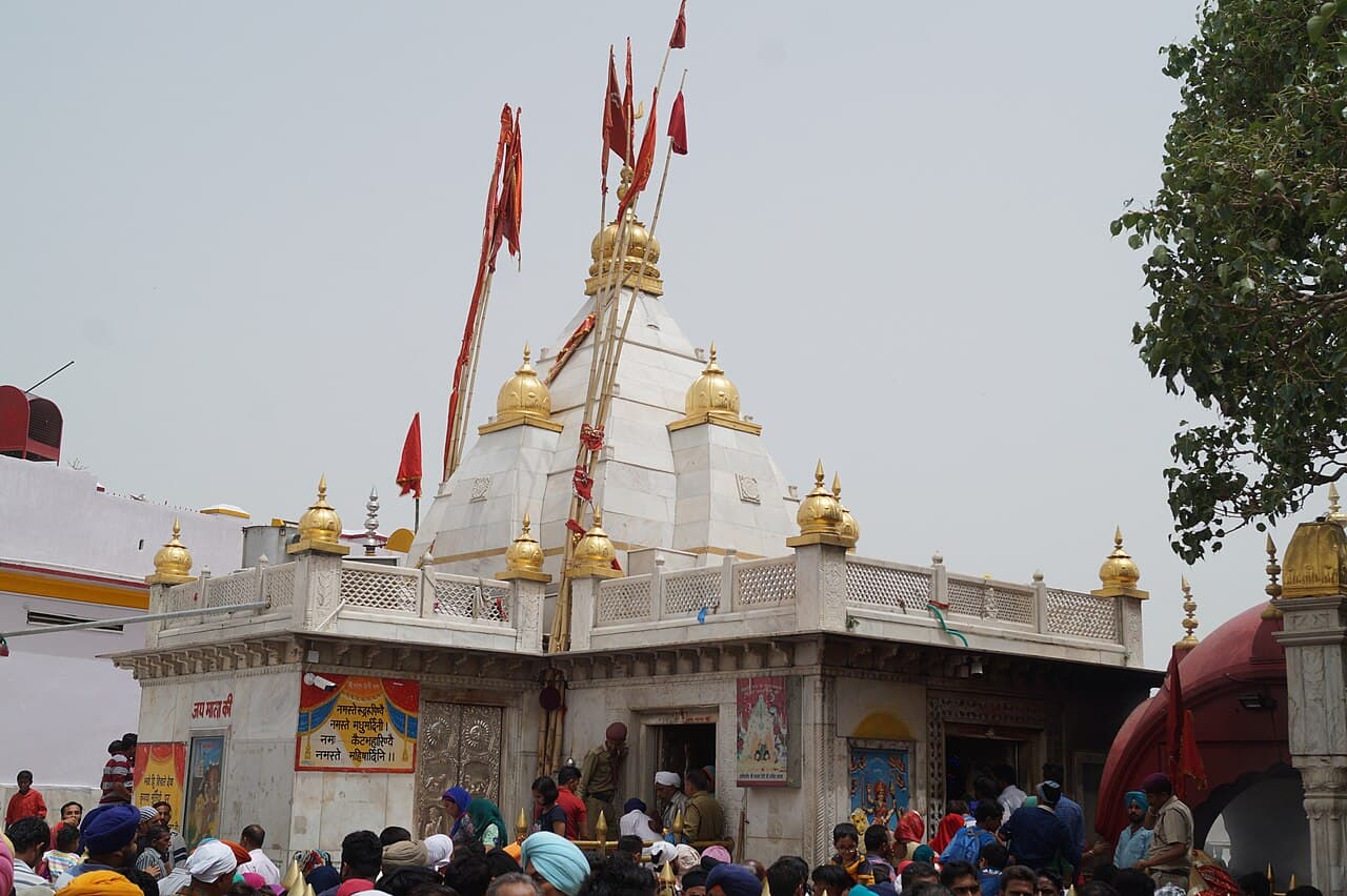 Shri Naina Devi Ji on its Bilaspur ridge — the white marble shikhara under gilded kalashas, red dhwajas over the doorway and pilgrims crowding the threshold