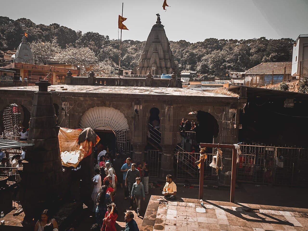 The Bhimashankar temple in its Sahyadri hollow — the Nagara shikhara and dhwaja rising behind the stone sabhamandapa, pilgrims crossing the courtyard below