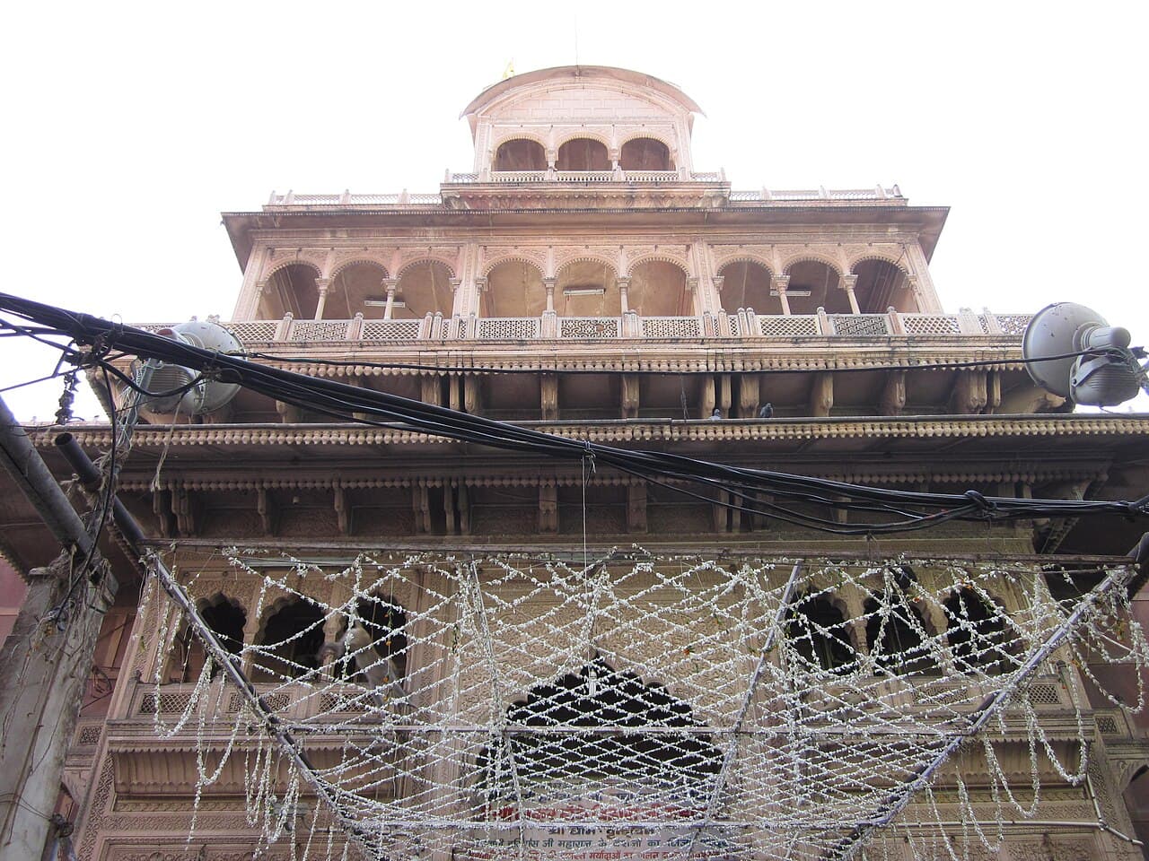 The carved sandstone front of Shri Banke Bihari Mandir rising in tiers of arcaded galleries above its Vrindavan lane, strung with flowers