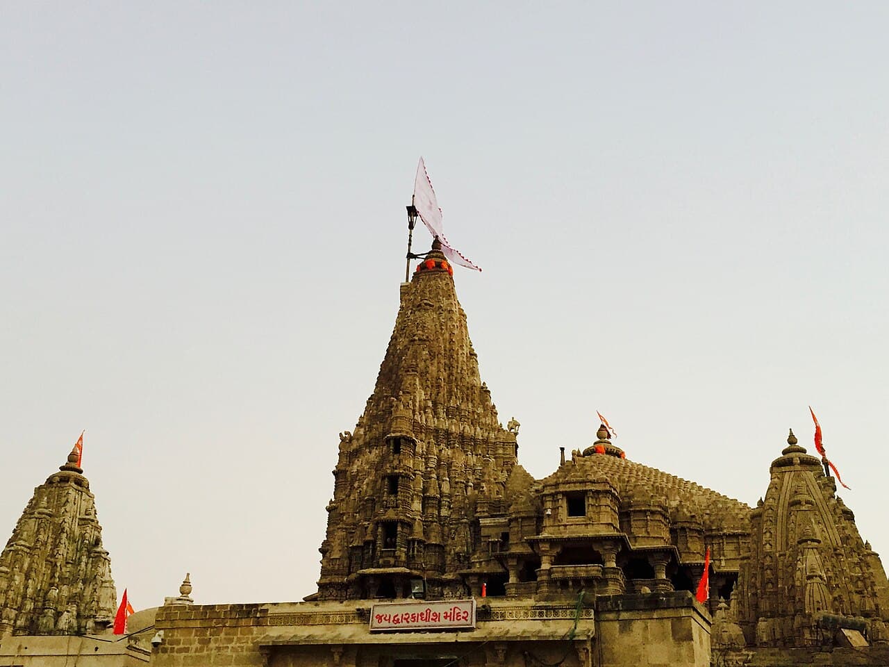 The Jagat Mandir at Dwarka — the tall carved shikhara of Dwarkadhish under its dhwaja, subsidiary spires and saffron flags along the compound wall