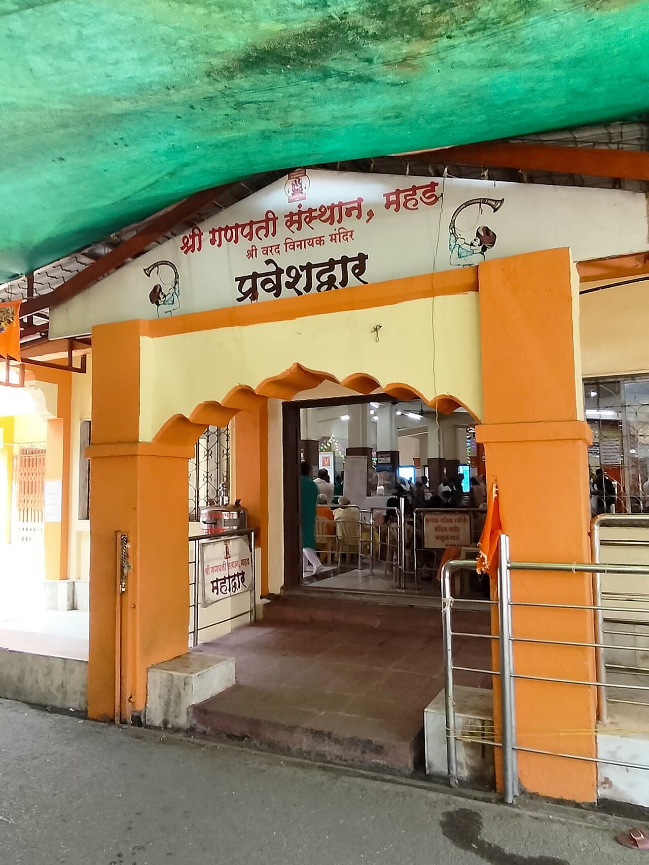 The saffron-and-cream pravesh-dwar of Shri Varadvinayak Mandir at Mahad, the Ganapati Sansthan's Marathi name board above the arch and the darshan hall beyond